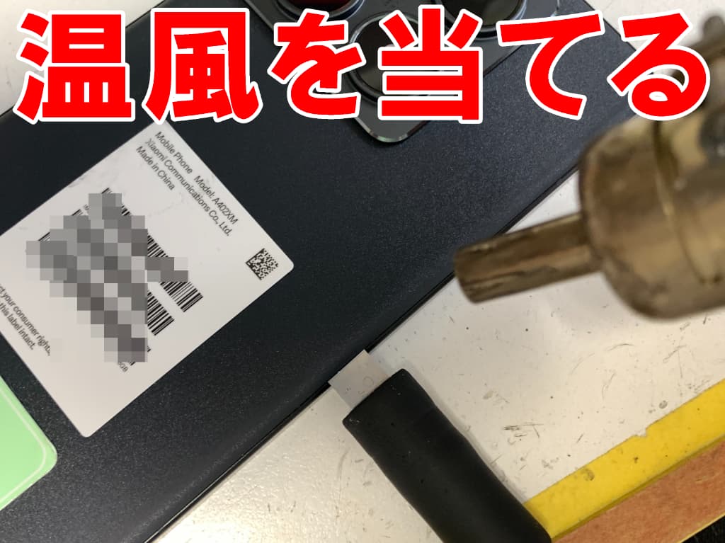 背面パネルに温風を当てて粘着を弱めている水没修理中の14T Pro
