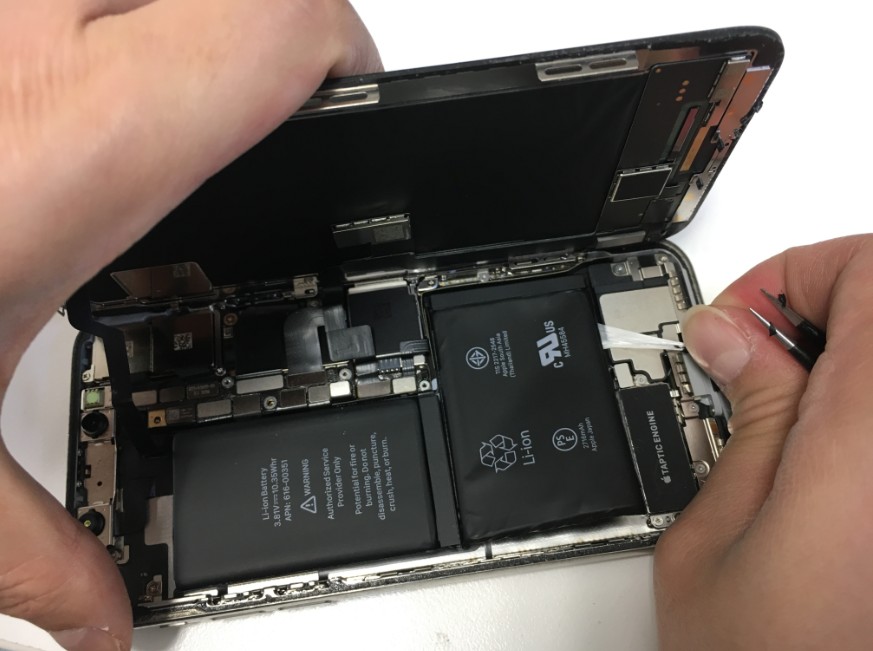 iPhoneXのバッテリー固定シール本体下部右端を引っ張っている