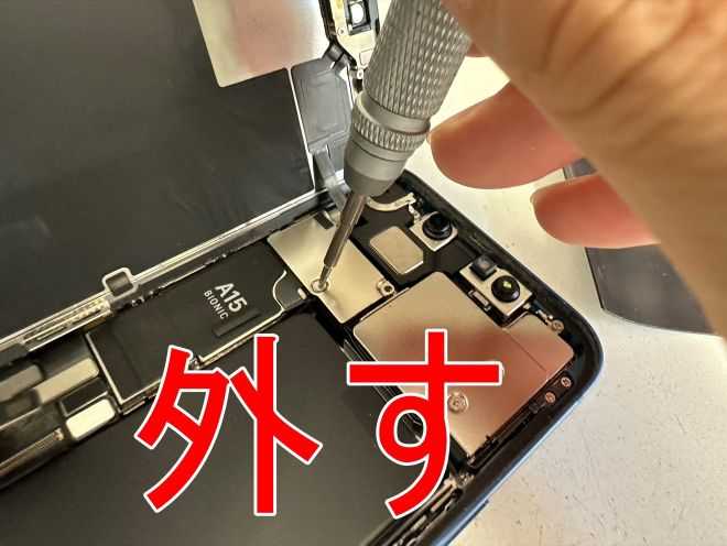 FaceIDセンサーのコネクタを固定した銀板のネジを外しているiPhone13mini