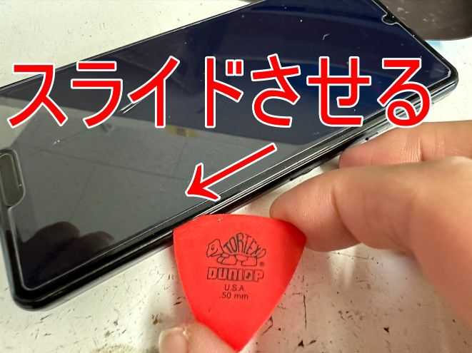 画面と本体フレームとの間に挟んだピックをスライドさせて画面パーツと本体フレームとの粘着を切っているAQUOS sense5G