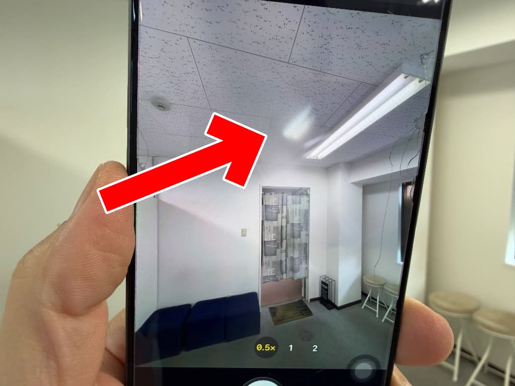 カメラレンズに光が反射して白い幻影が映っているiPhone16